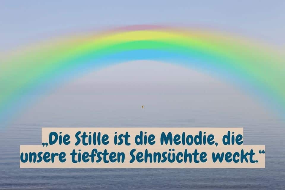 Regenbogen über dem Meer und Spruch: „Die Stille ist die Melodie, die unsere tiefsten Sehnsüchte weckt.“