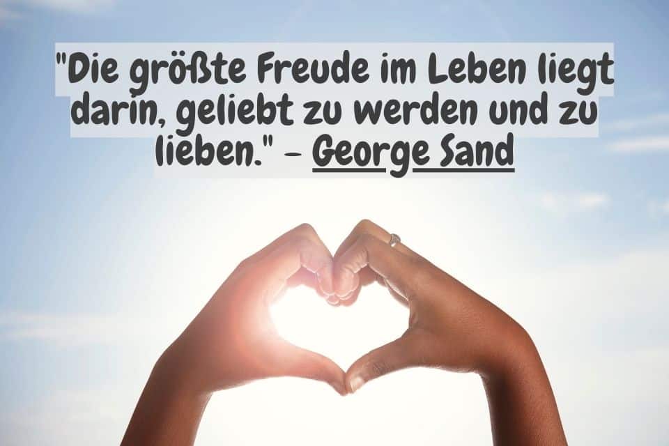 Mit Händen geformtes Herz und Spruch: "Die größte Freude im Leben liegt darin, geliebt zu werden und zu lieben." - George Sand