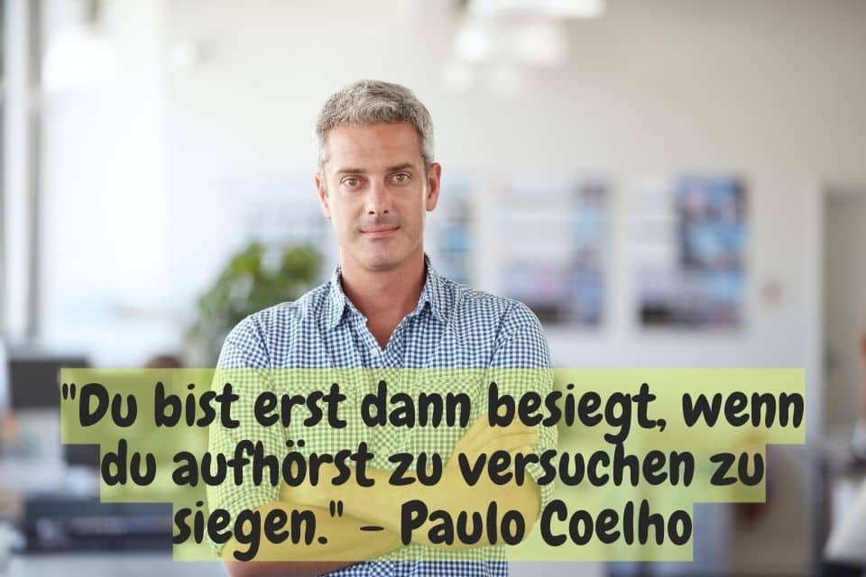 Mann mit verschränkten Armen und Zitat: "Du bist erst dann besiegt, wenn du aufhörst zu versuchen zu siegen." - Paulo Coelho