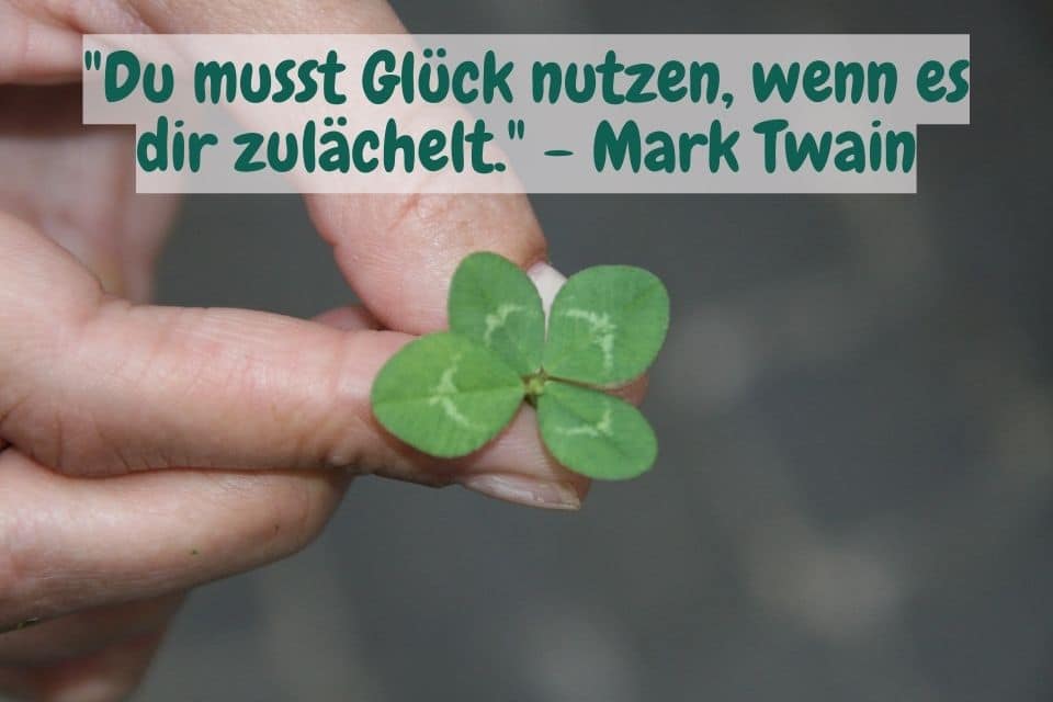 Eine Hand hält ein vierblätteriges Kleeblatt und Zitat: "Du musst Glück nutzen, wenn es dir zulächelt." - Mark Twain