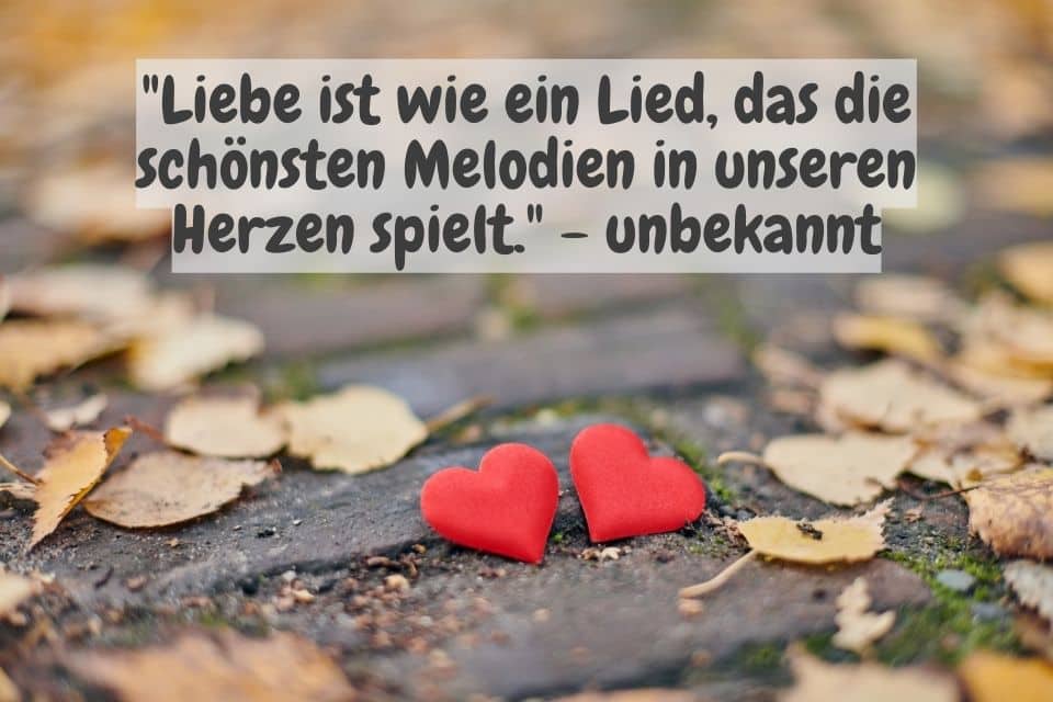Zwei rote Herzen im Laub und Spruch: "Liebe ist wie ein Lied, das die schönsten Melodien in unseren Herzen spielt." - unbekannt