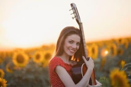 Una donna con una chitarra in un campo di girasoli: cosa porta la musica in medicina