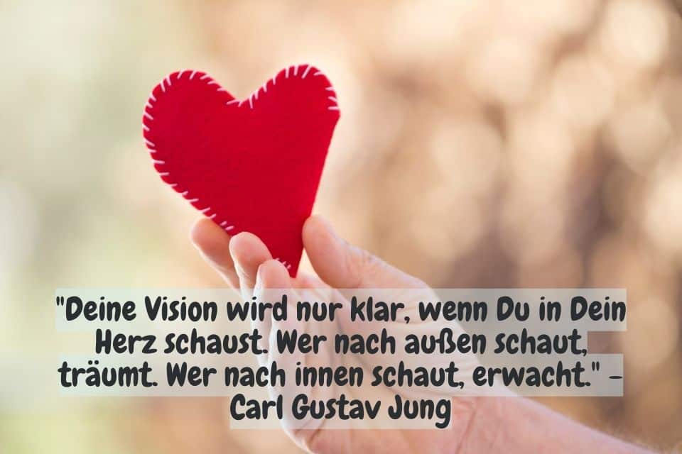Eine Hand hält ein rotes Soff Herz in die Luft, mit Zitat: "Deine Vision wird nur klar, wenn Du in Dein Herz schaust. Wer nach außen schaut, träumt. Wer nach innen schaut, erwacht." - Carl Gustav Jung